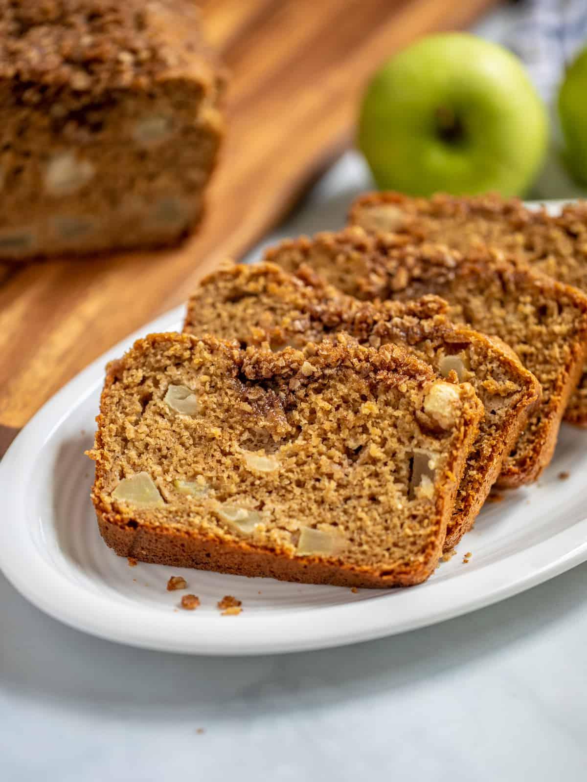 Apfelbrot Geschnittenes Apfelbrot mit Streuseln auf weißer Platte mit Granny Smith Äpfeln im Hintergrund.
