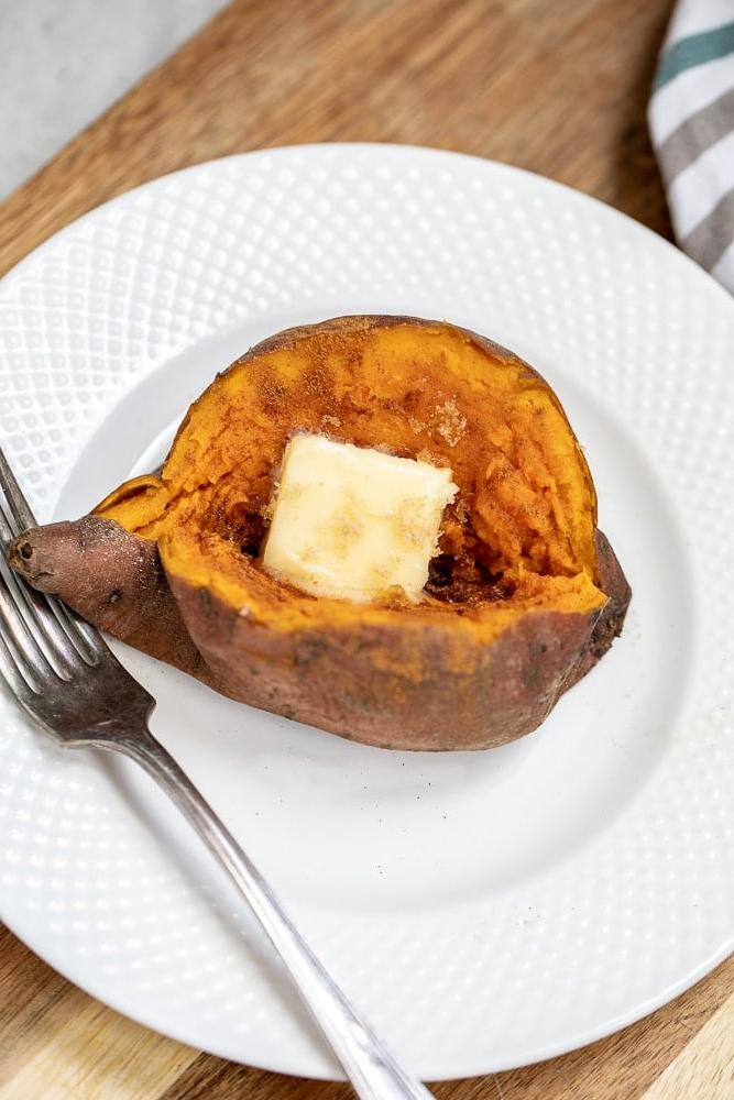 Auf einem weißen Teller angerichtete gebackene Süßkartoffel, mit Butter und Zimt bestreut.