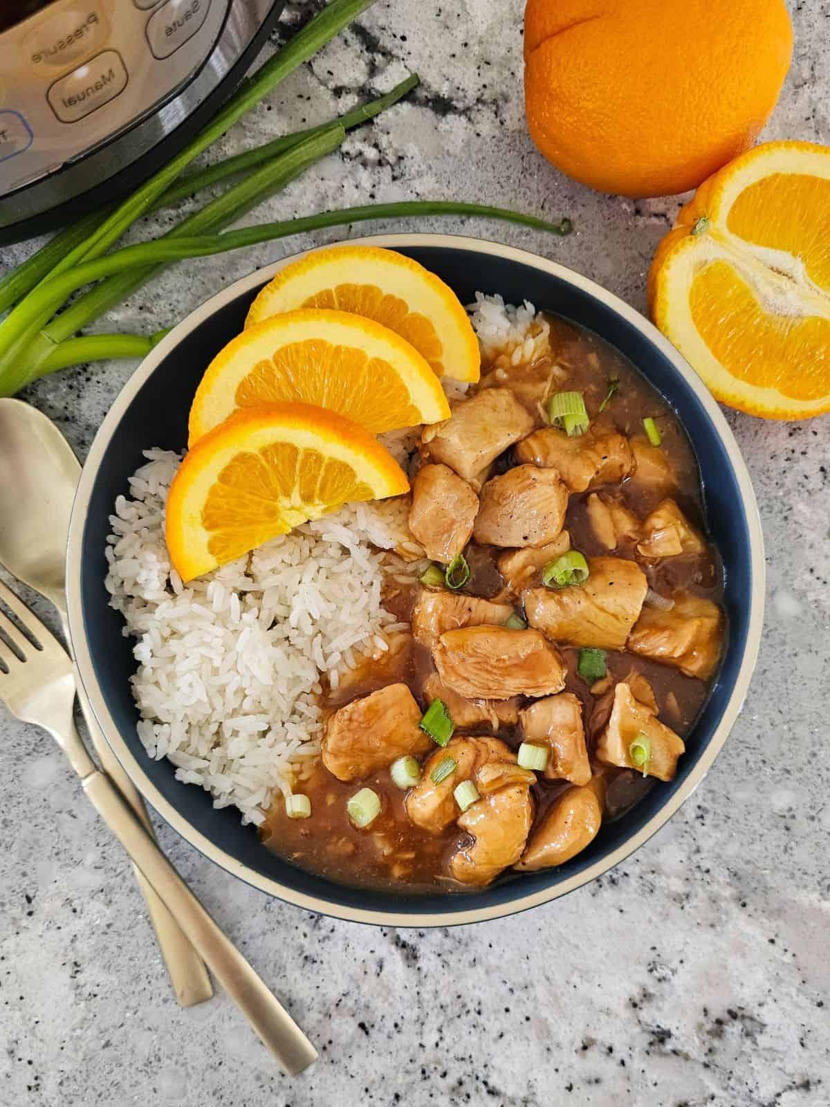Instant Pot Orangen-Hähnchen serviert mit Reis und frischen Orangen im Hintergrund.
