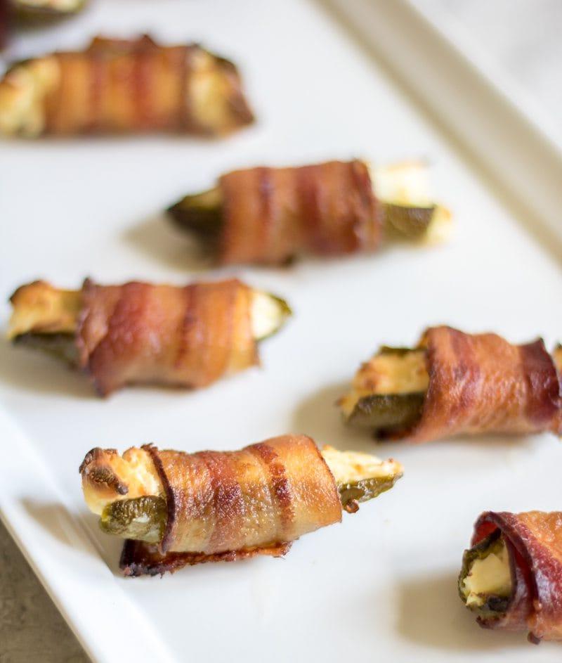 Gegrillte Jalapeño Poppers im Speckmantel auf weißer Platte, bereit zum Servieren.