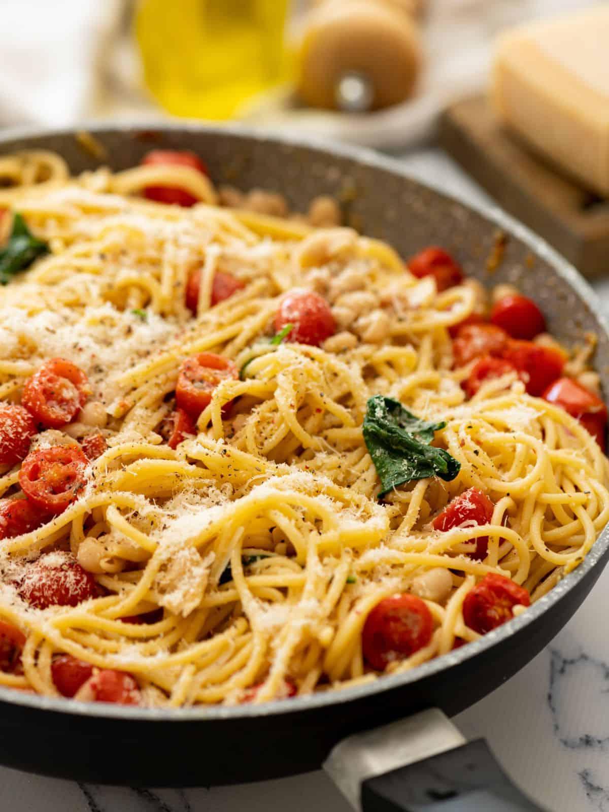 Große Pfanne mit Pasta, weißen Bohnen, Tomaten und Spinat, mit Parmesan bestreut.