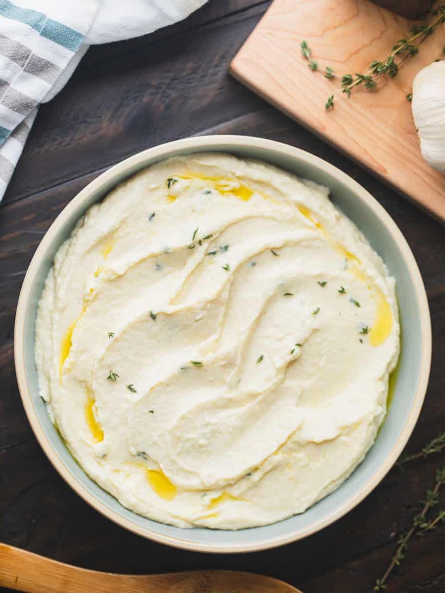 Pastinakenpüree Rezept Eine Schale mit cremigem Pastinakenpüree mit Knoblauch und Meerrettich, beträufelt mit Olivenöl und garniert mit frischen Thymianblättern.