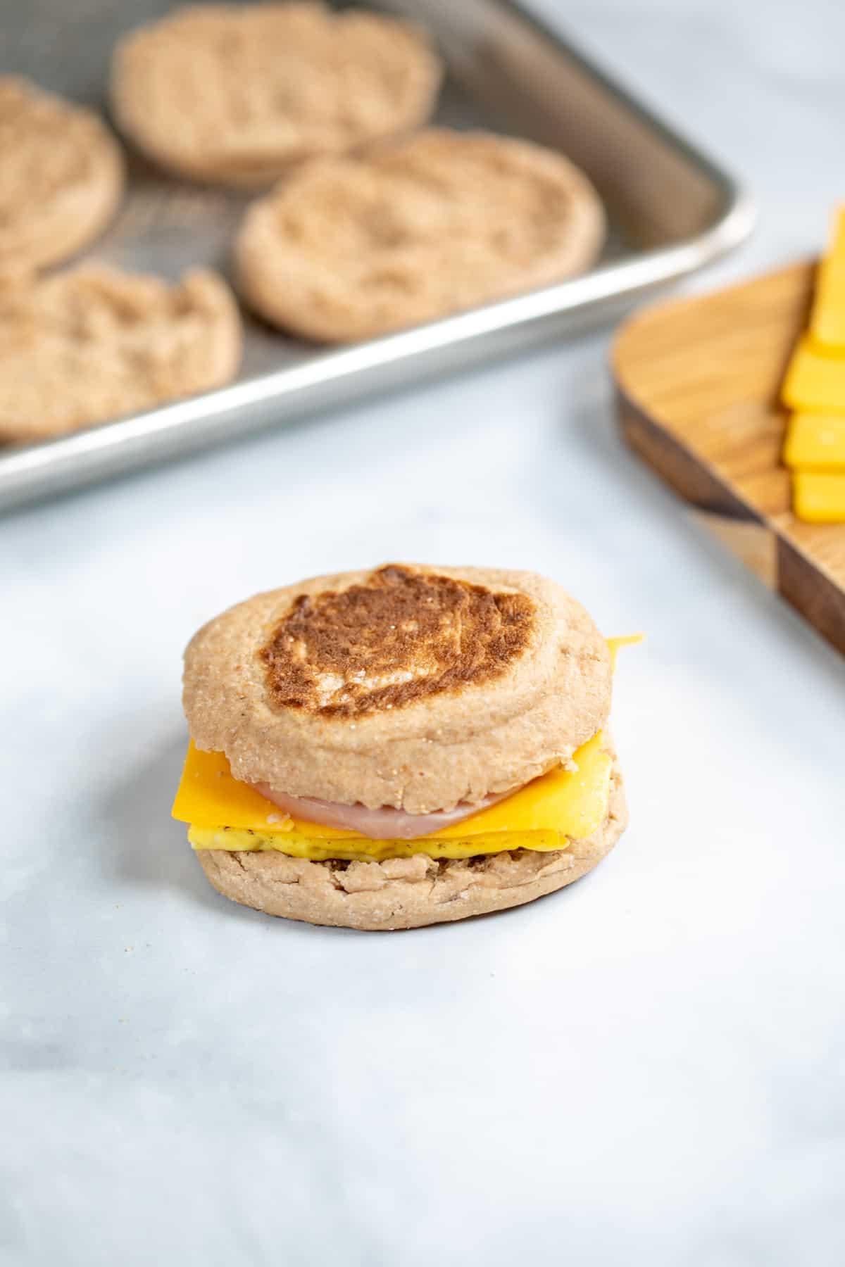 Zusammengestellter Egg McMuffin neben getoasteten English Muffins.