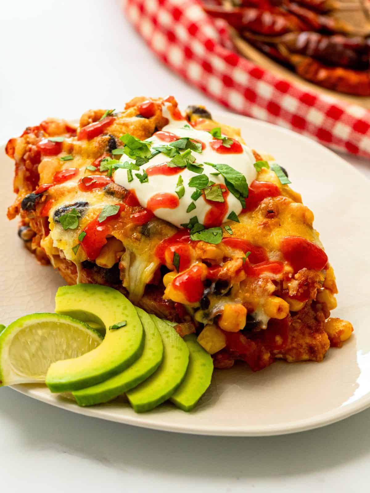 Cowboy Hähnchen Rezept Cowboy Hähnchen Auflauf auf weißem Teller serviert, mit Sauerrahm, Koriander, Avocadoscheiben und Limettenspalte.
