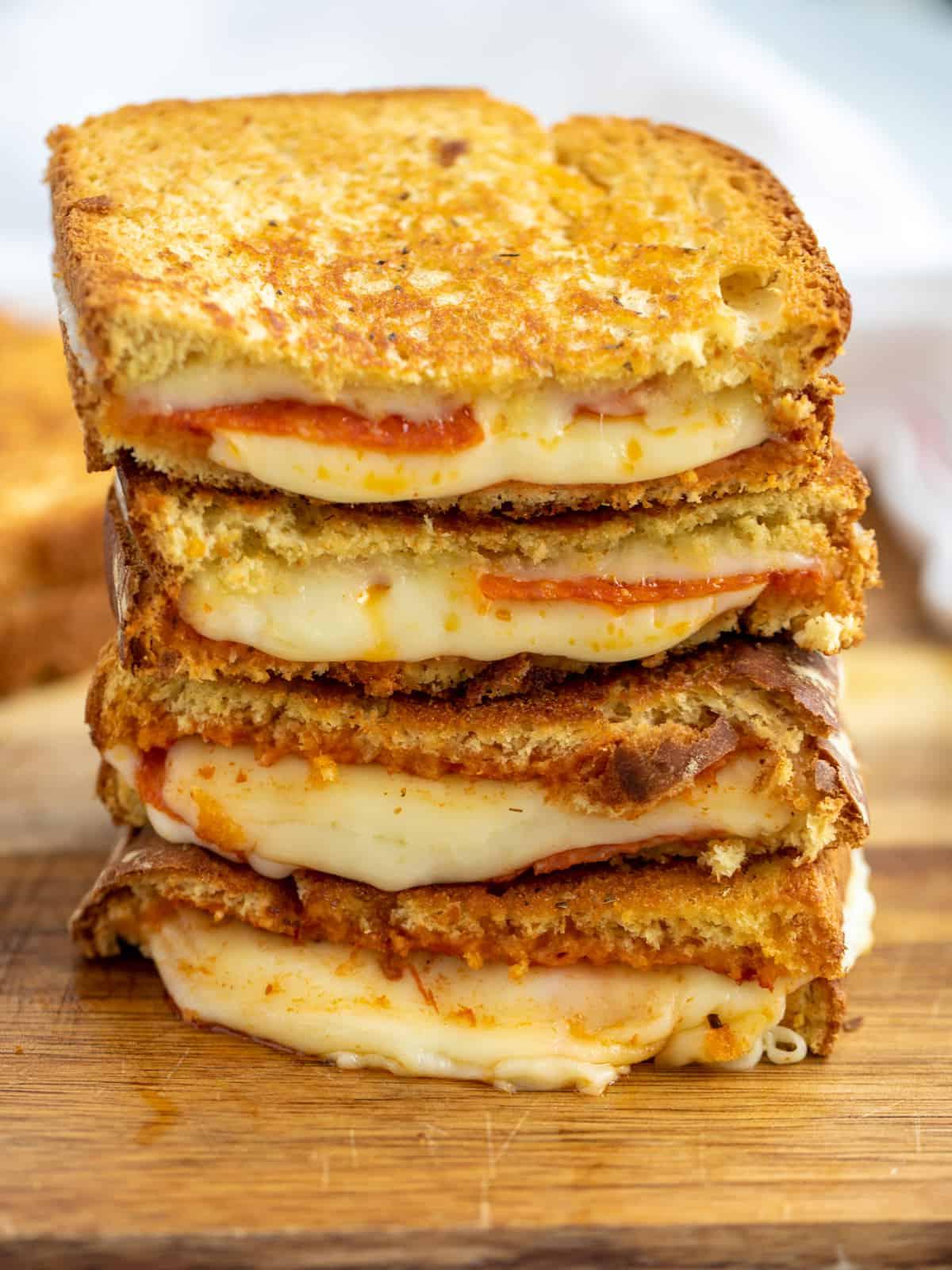 Aufgeschnittener Stapel Pizza Grilled Cheese, aus dem Käse auf einem Schneidebrett quillt.