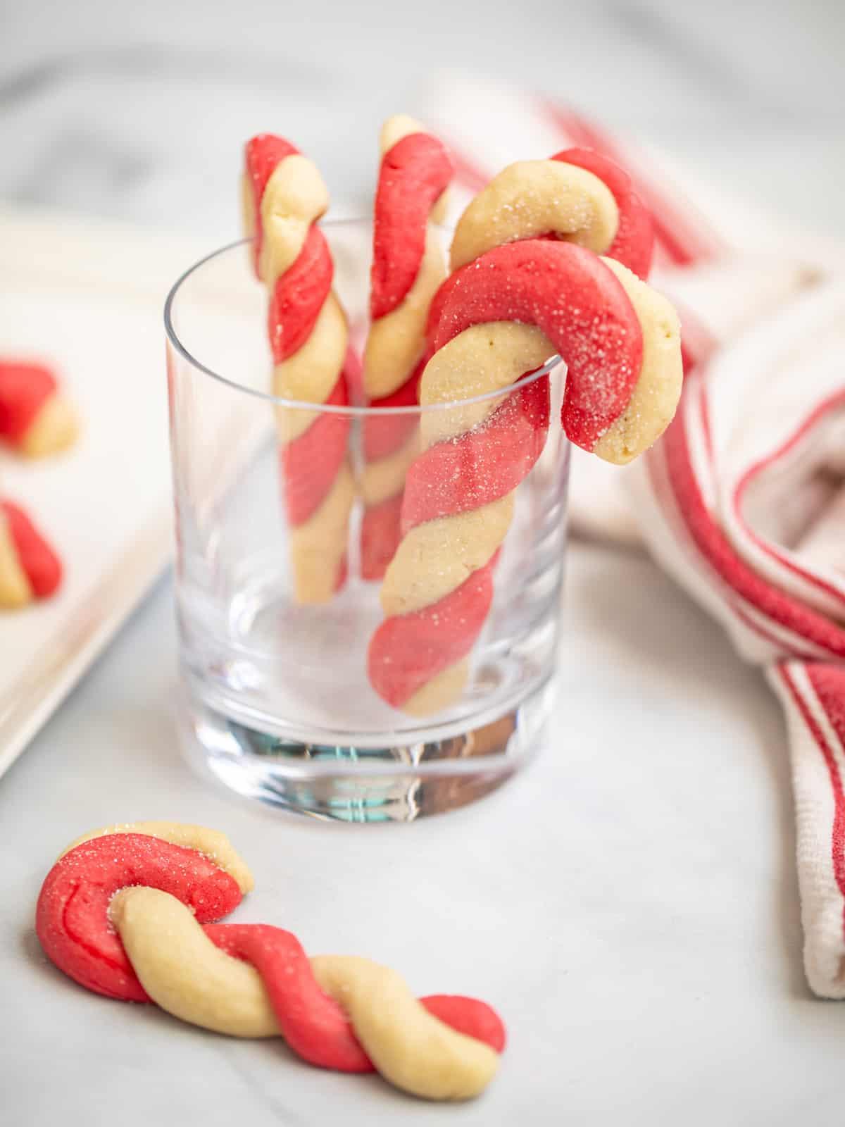 Transparente Zuckerstangen-Plätzchen, die an einem Trinkglas hängen, mit einem gebackenen Plätzchen davor.