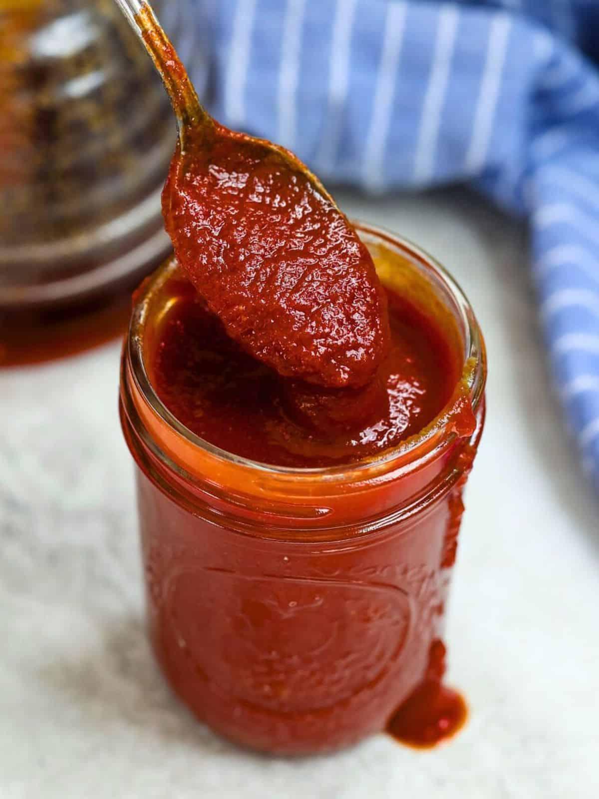 Ein Glas selbstgemachter BBQ-Sauce mit einem Löffel, der herausragt.