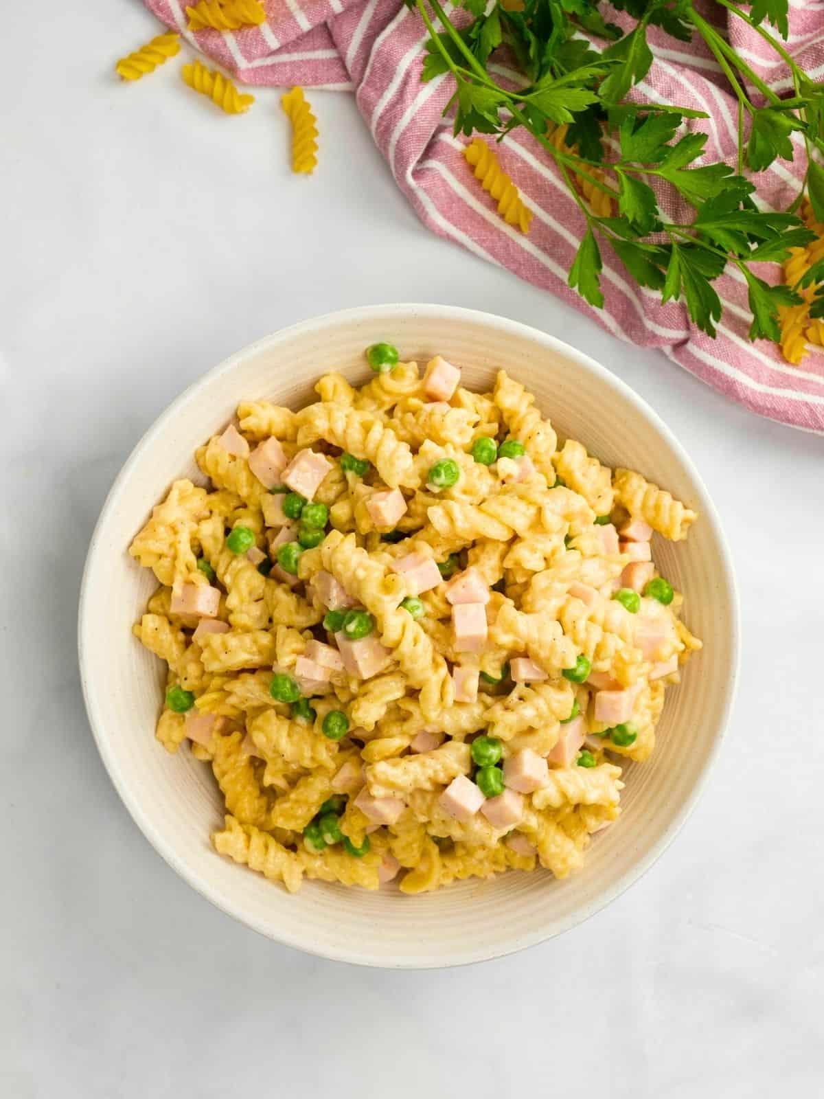 Eine Schüssel cremiger Instant Pot Schinken-Käse-Pasta mit Rotini-Nudeln im Hintergrund.