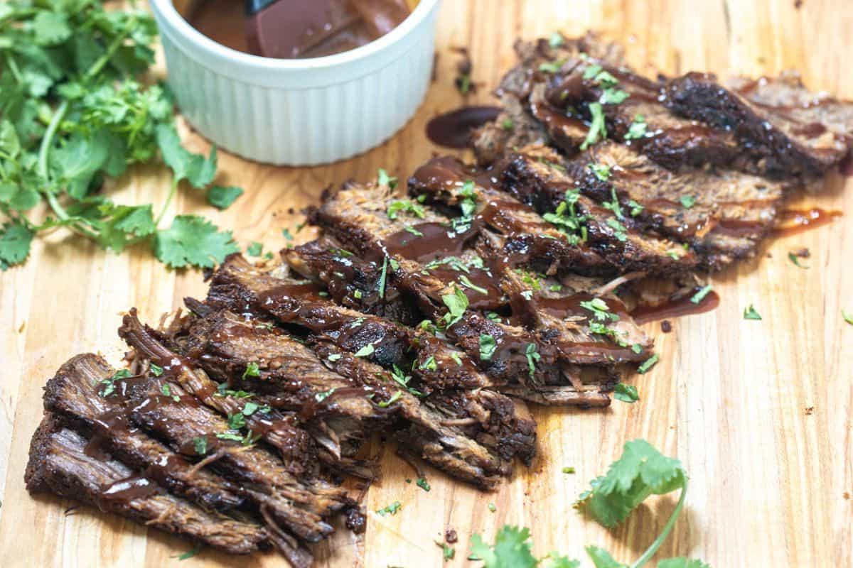 Geschnittenes Instant Pot Brisket auf einem Holzschneidebrett, beträufelt mit BBQ-Sauce und Petersilie an der Seite.