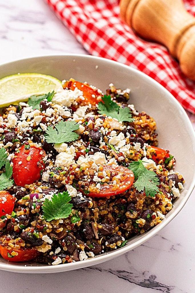 Glutenfreier Mexikanischer Quinoa Salat in einer weißen Schüssel, garniert mit Feta und Kirschtomaten.