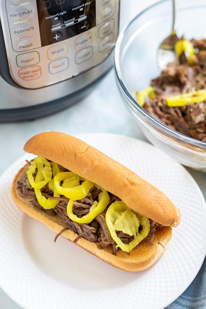 Schüssel mit geschreddertem Instant Pot Italienischem Rindfleisch neben einem Italian Beef Sandwich und einem Instant Pot.