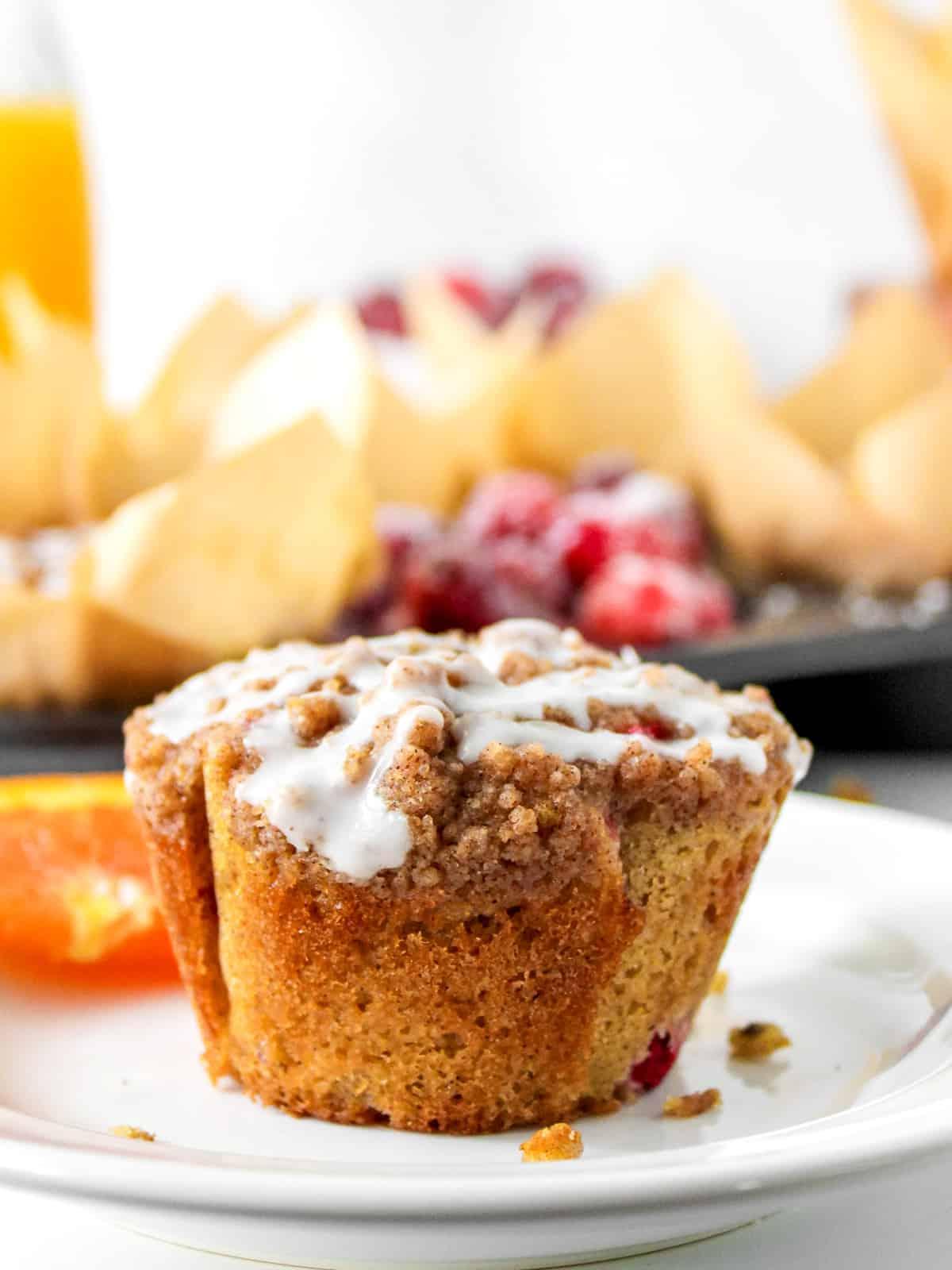 Weiche, saftige Cranberry-Orangen-Muffins auf einem weißen Teller neben einer frischen Orange.