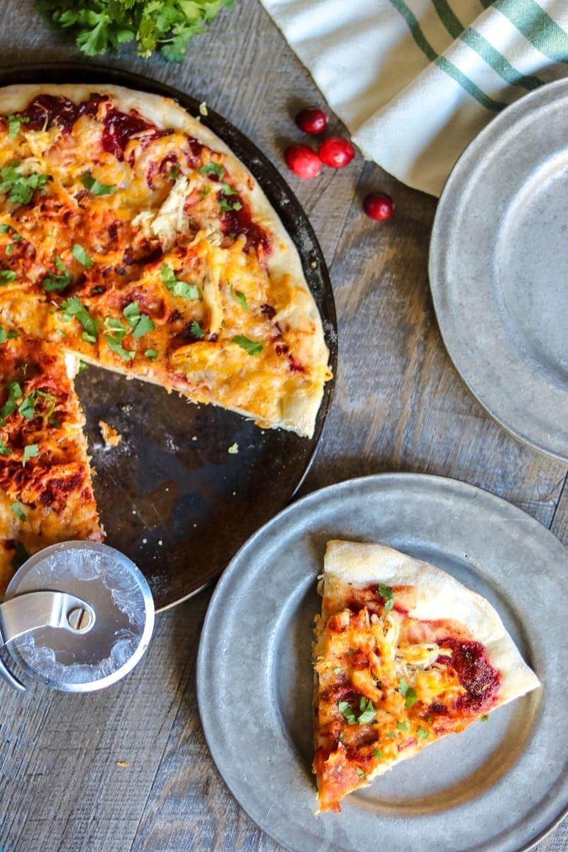 Pizzablech mit Preiselbeer-Truthahn-BBQ-Pizza, ein Stück auf einem silbernen Teller.