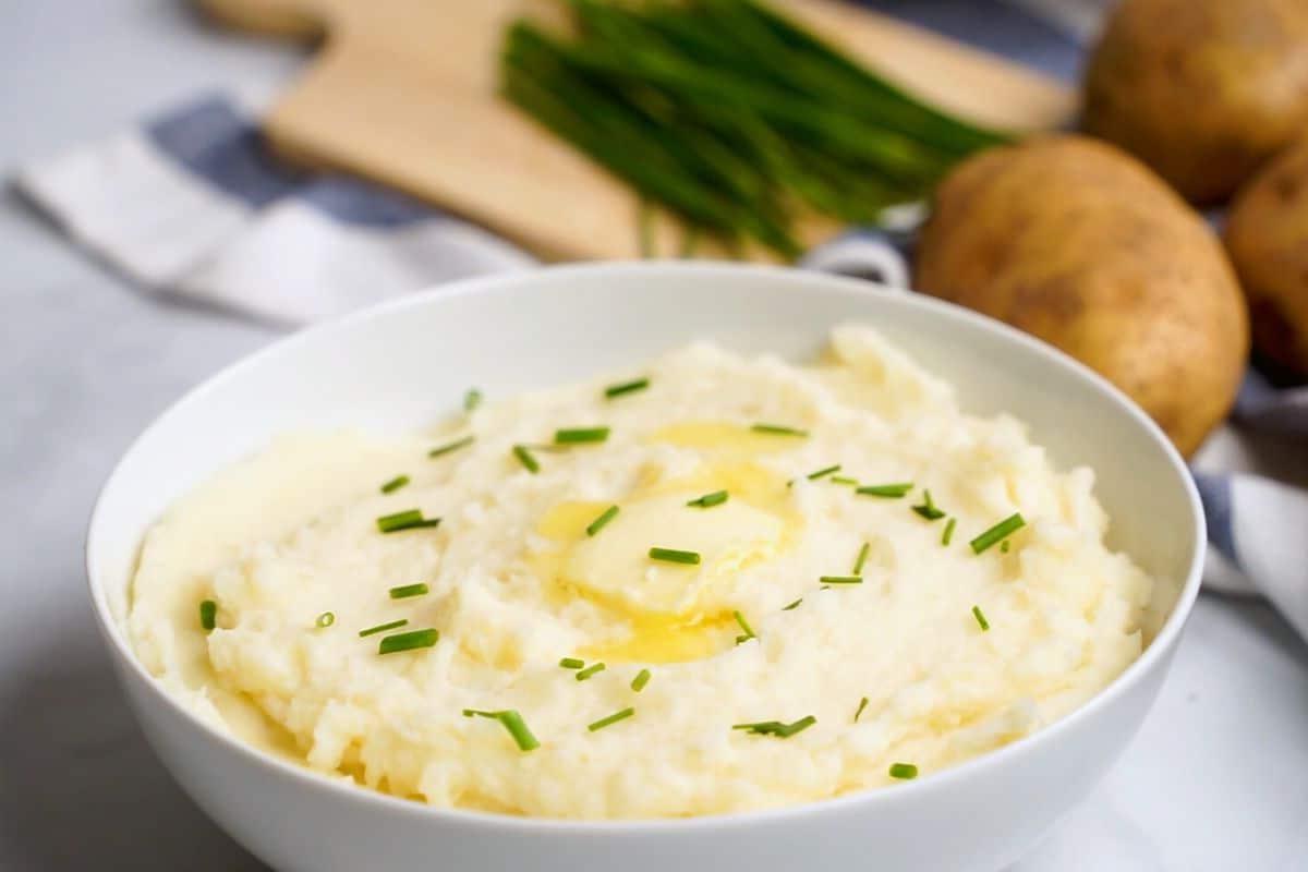 Schüssel mit cremigem Instant Pot Kartoffelpüree, garniert mit Butter und Schnittlauch in einer weißen Schüssel.