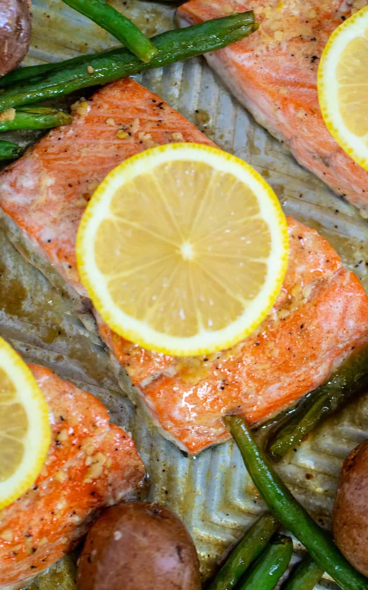 Lachs auf dem Backblech, bedeckt mit geschnittenem Lachs, daneben grüne Bohnen und Kartoffeln. Nahaufnahme.