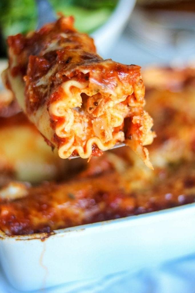 Ein Metallspatel, der Lasagne-Röllchen aus einer Auflaufform hebt.