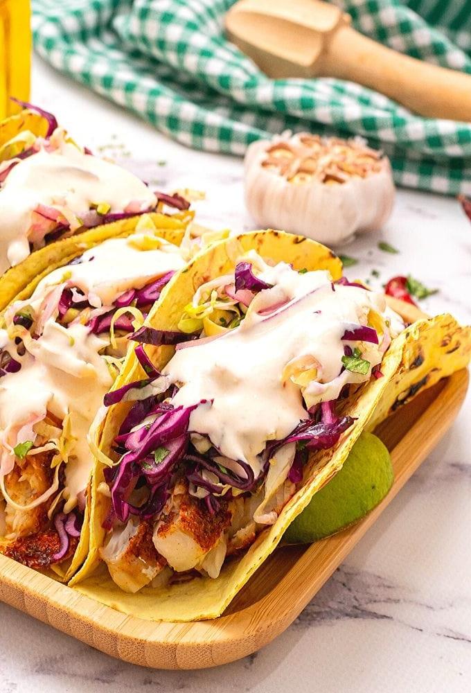 Fisch Tacos mit Krautsalat und Chipotle-Soße auf einem Holztablett mit Limetten im Hintergrund. 
