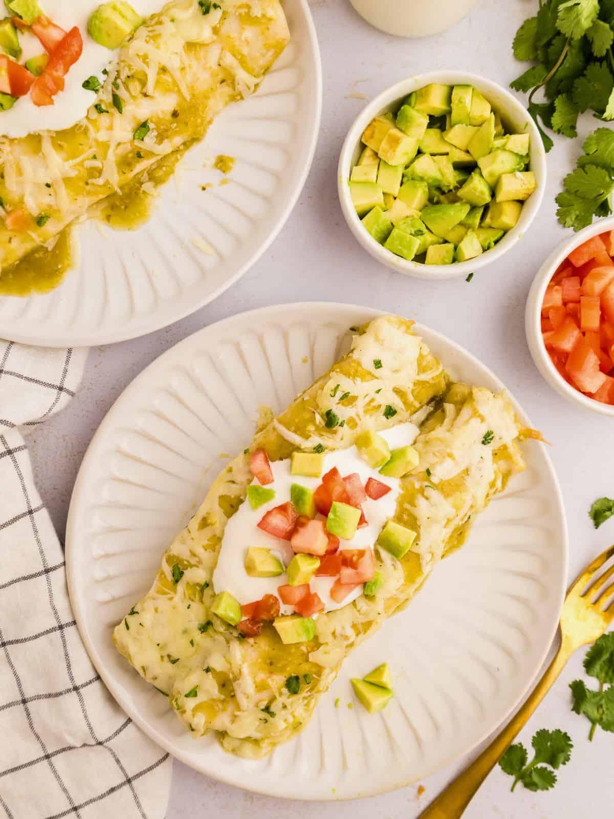 Grüne Salsa Verde Enchiladas mit Hähnchen auf weißem Teller, garniert mit gewürfelten Avocado und Tomaten.