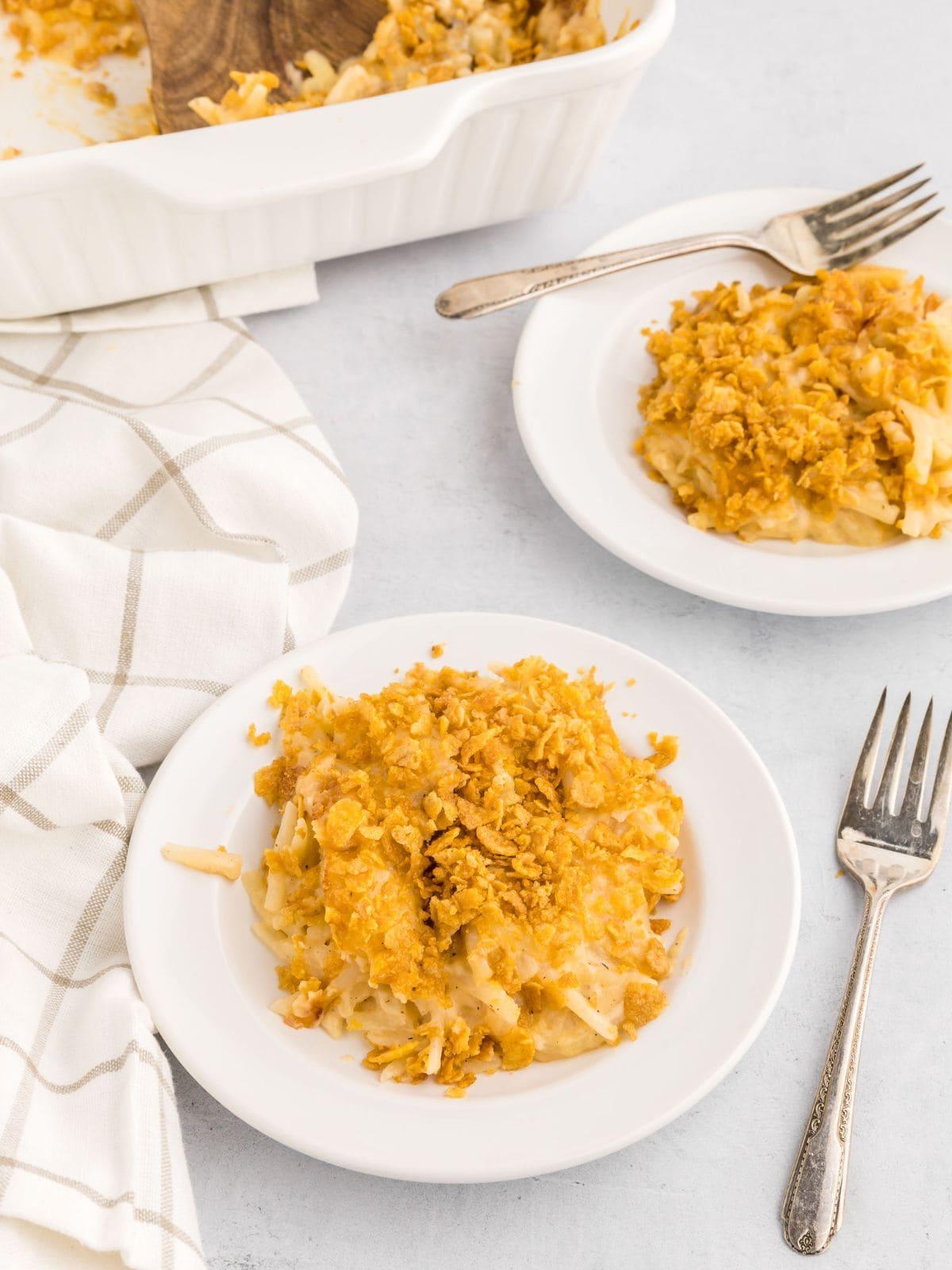 Cremiger Käse-Kartoffelauflauf Funeral Potatoes auf einem weißen Teller angerichtet, daneben eine Gabel.