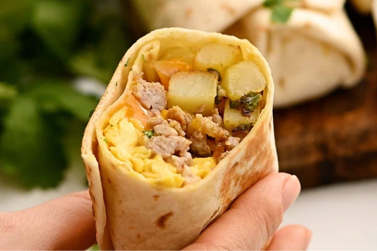 Aufgeschnittener Frühstücks-Burrito mit sichtbaren Eiern, Wurst und Kartoffeln im Inneren.