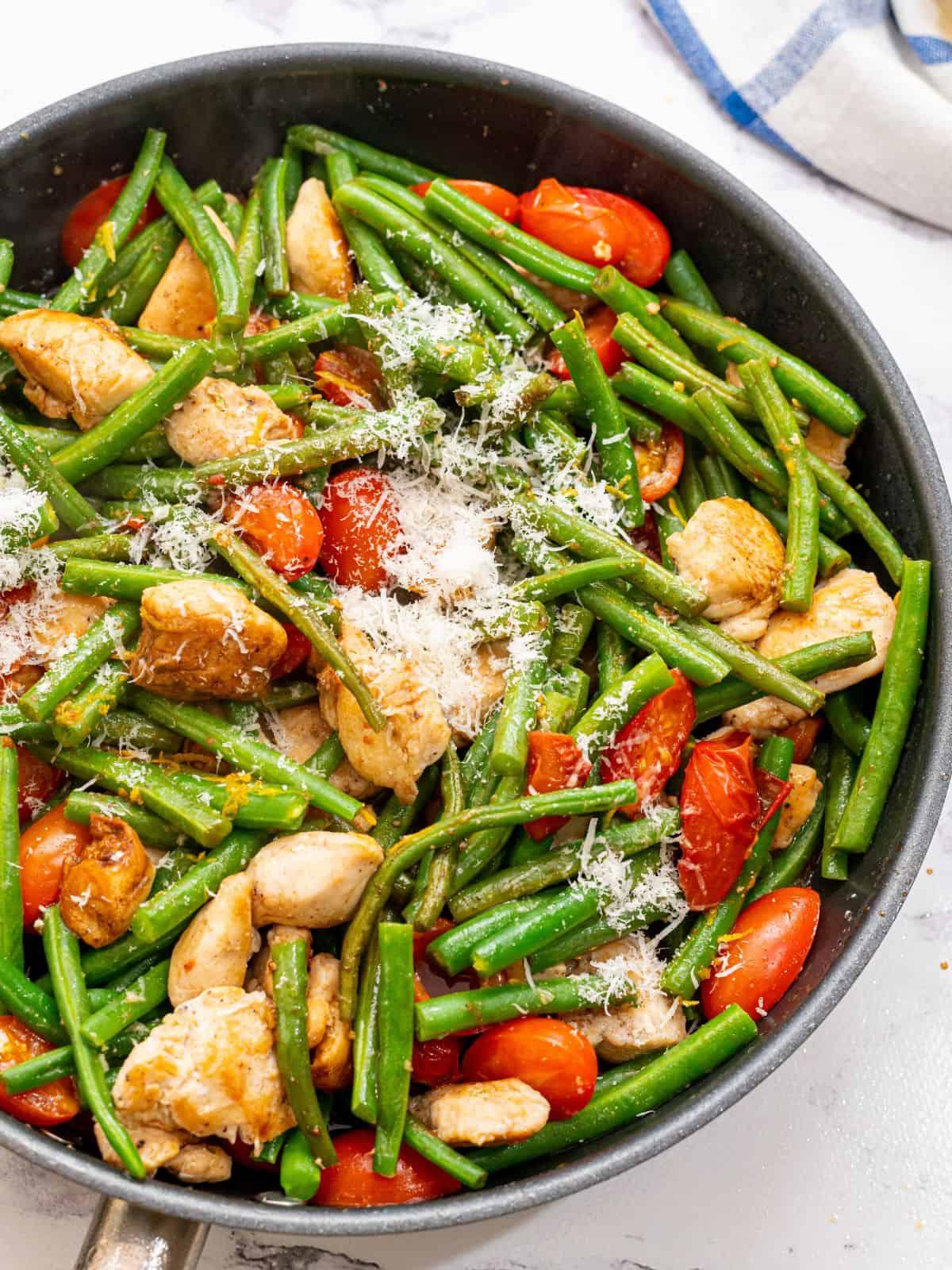Große Pfanne mit Hähnchenstücken, grünen Bohnen, Kirschtomaten und Parmesan.