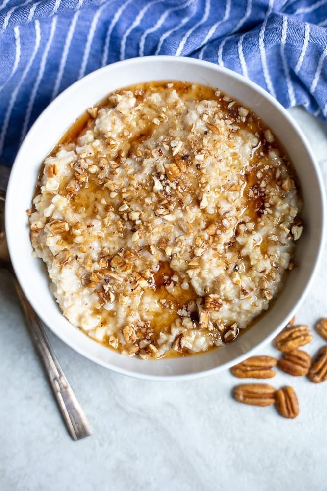 Eine Schüssel cremiger Slow Cooker Haferbrei in einer weißen Schüssel, garniert mit Pekannüssen und Ahornsirup