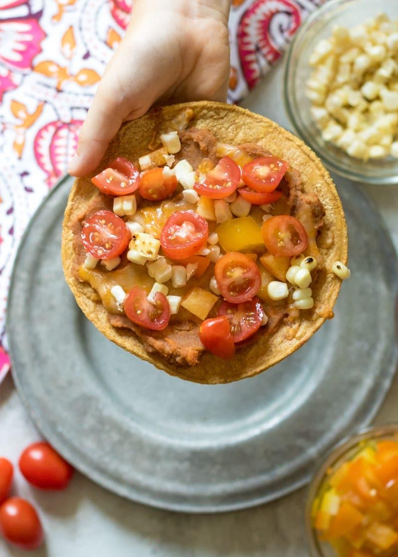 Kinderhand hält eine gebackene Tostada, belegt mit Tomaten und Mais.
