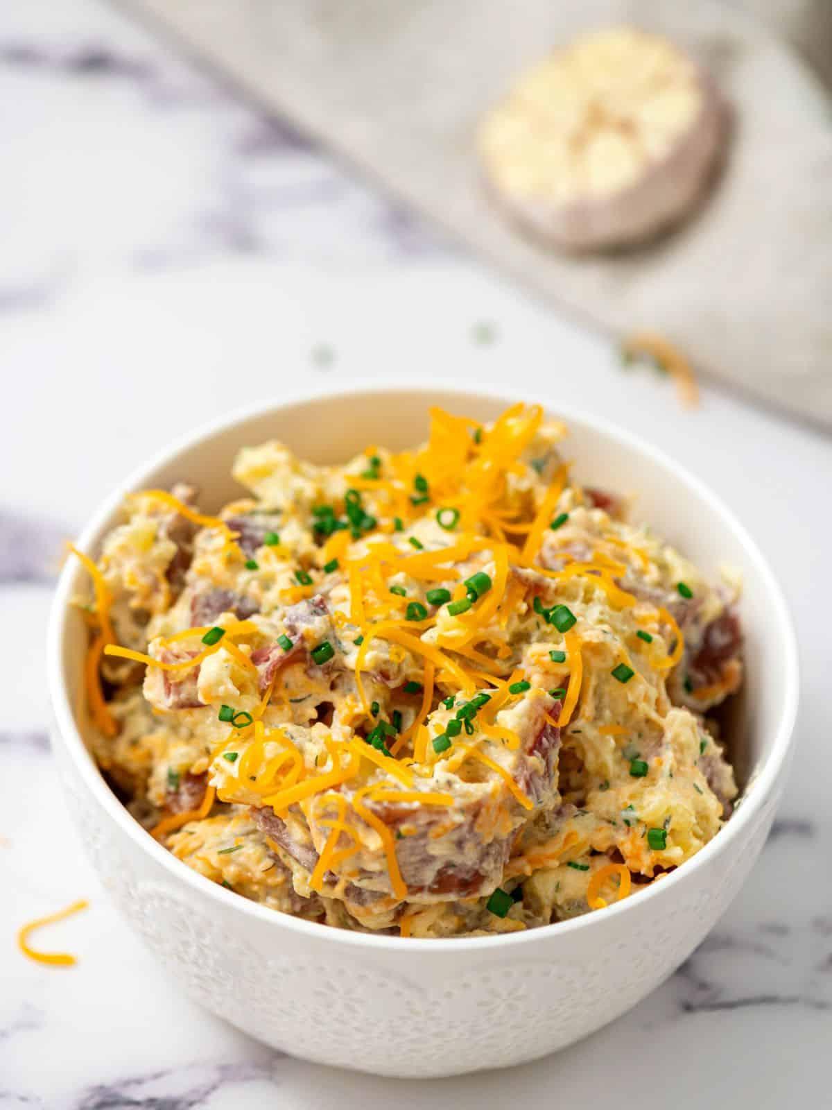 Ranch Kartoffelsalat mit roten Kartoffeln und Speck in einer weißen Servierschale, garniert mit Cheddar und Schnittlauch.