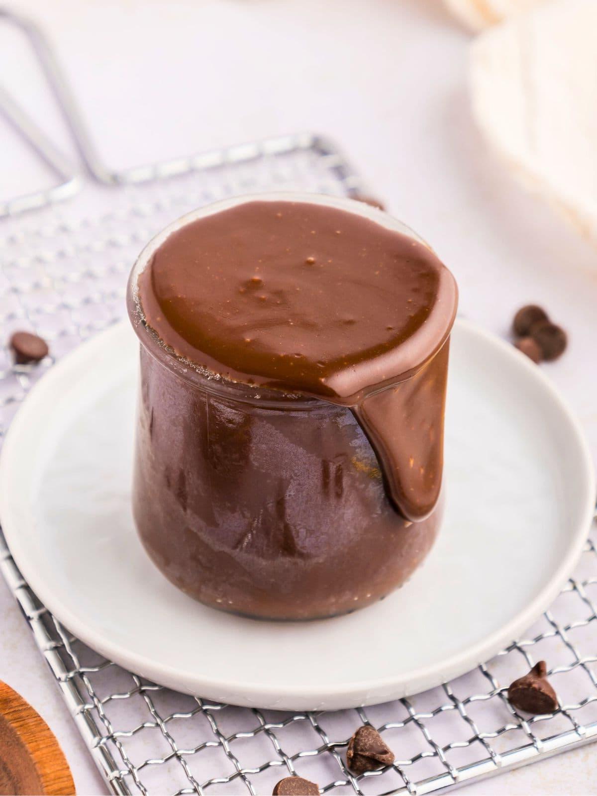 Ein kleines Glas mit hausgemachter Hot Fudge Soße neben Schokoladenstückchen und Meersalz.