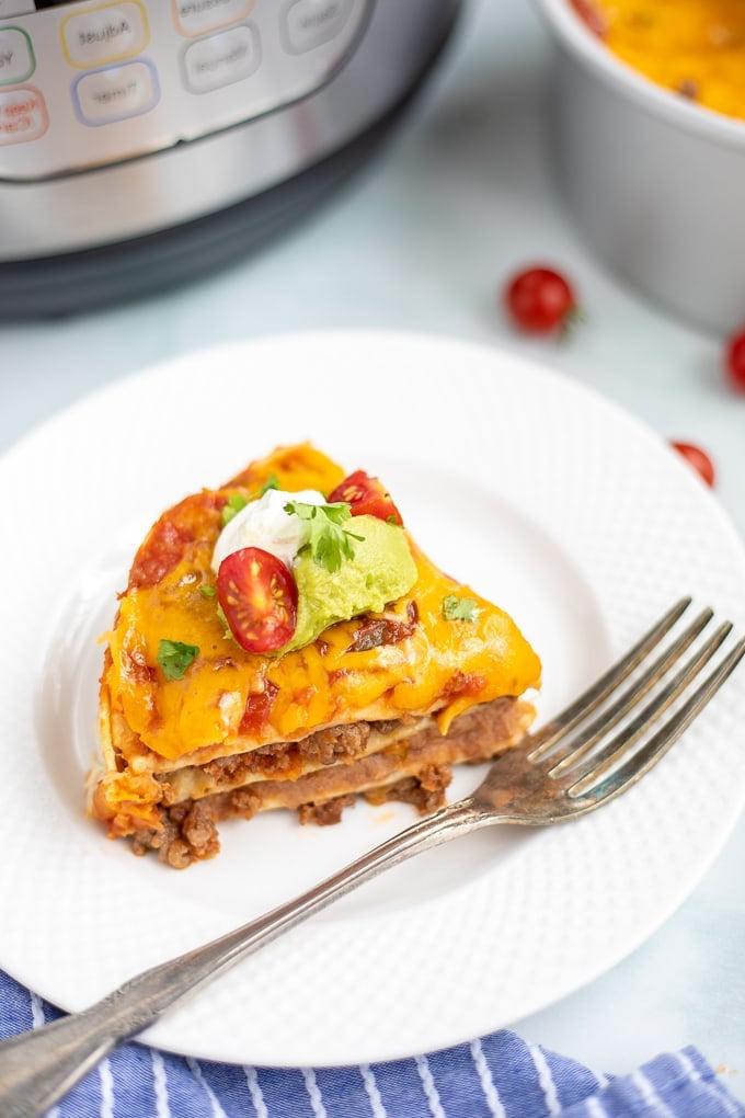 Ein Stück Instant Pot Mexican Lasagne auf einem weißen Teller mit einem Instant Pot im Hintergrund.