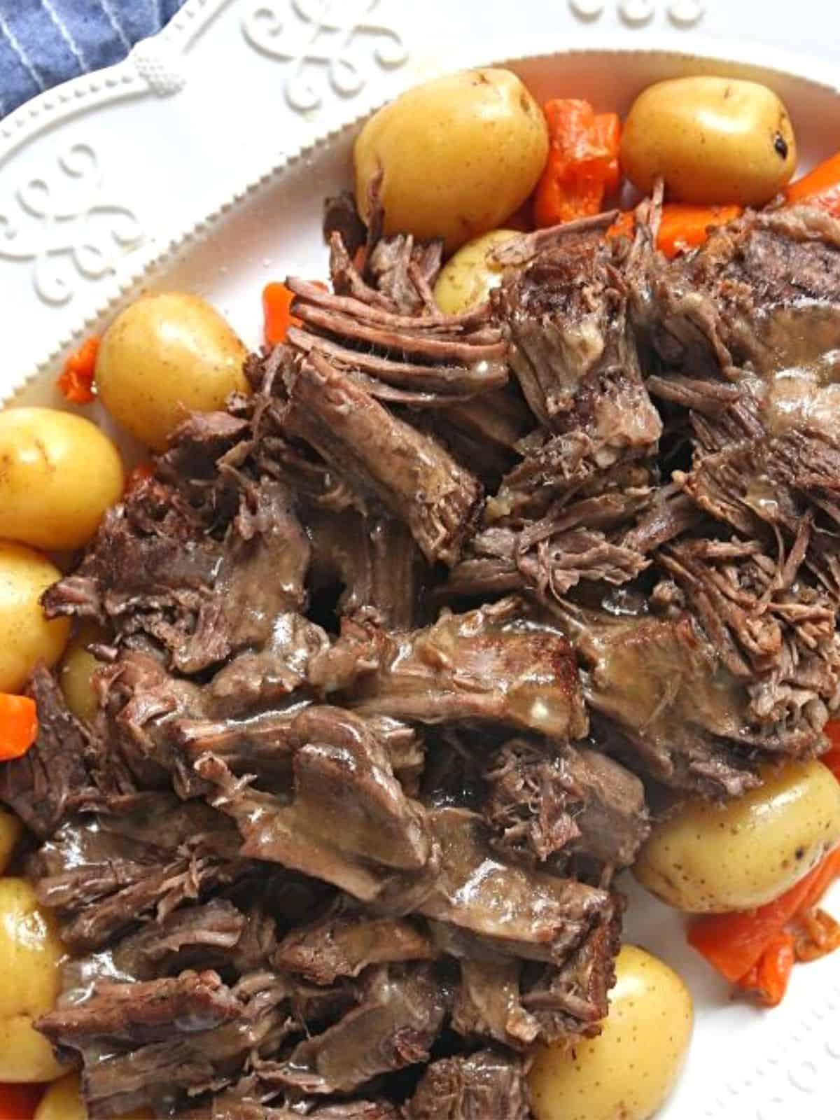 Ein köstlicher Schmorbraten auf einer weißen Servierplatte, umgeben von perfekt gegarten Kartoffeln und Karotten, daneben ein Instant Pot.
