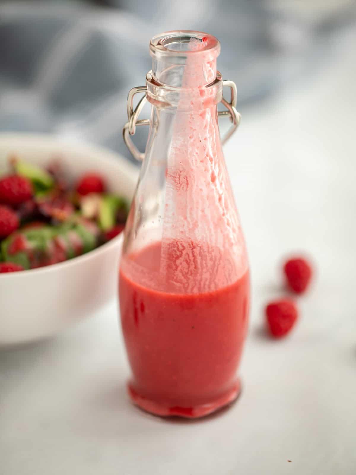 Flasche Himbeerdressing neben Salat mit Himbeeren.
