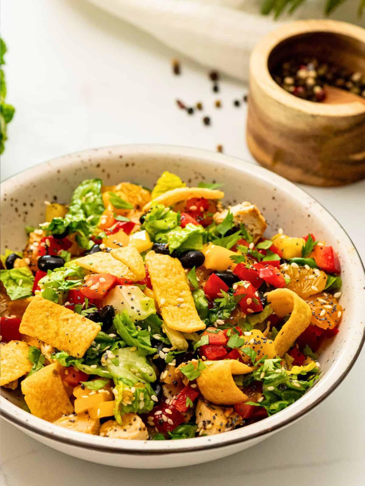 Karibischer Salat mit gegrilltem Hähnchen, schwarzen Bohnen, Ananas in weißer Schale, garniert mit Maischips.