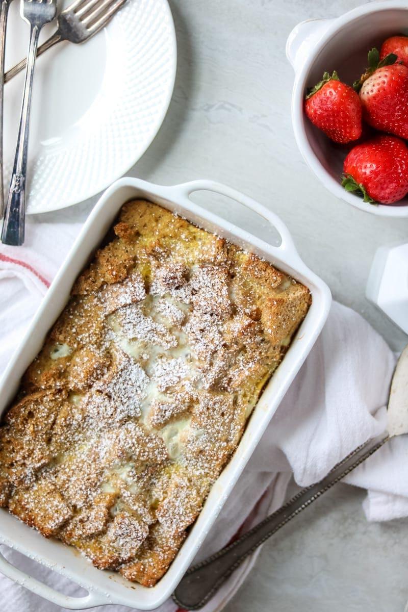 Gebackener Overnight Eierlikör French Toast Auflauf mit Erdbeeren, Bourbon-Glasur und Tellern daneben.