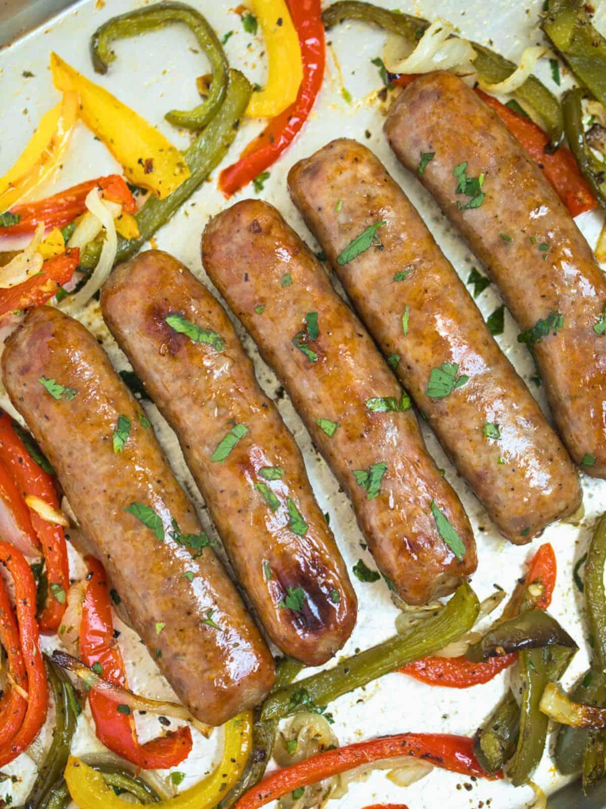 Ofengebackene italienische Würste mit Paprika und Zwiebeln, garniert mit gehackter Petersilie auf einem Backblech.