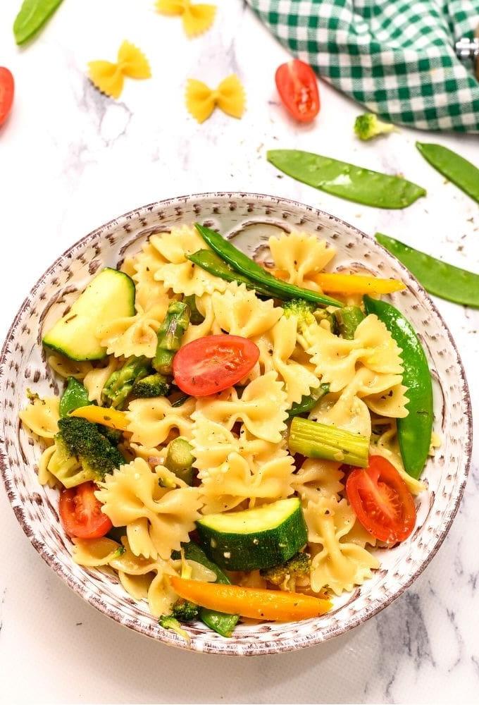 Frühlingshafte Pasta Primavera in einer Schüssel, daneben frische Zuckerschoten und Tomaten.