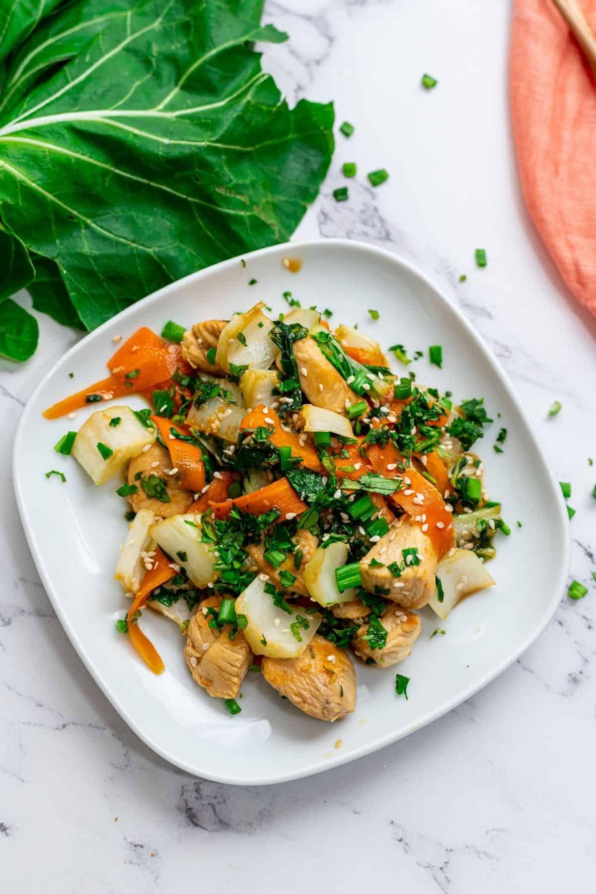 Teller mit Hähnchen- und Bok Choy-Stir-Fry neben frischem Bok Choy.