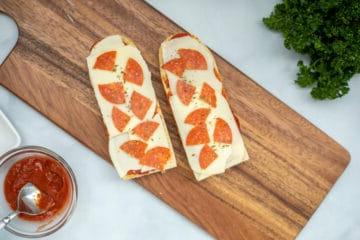 Zusammengesetzte Baguette Pizza auf einem Schneidebrett vor dem Frittieren.