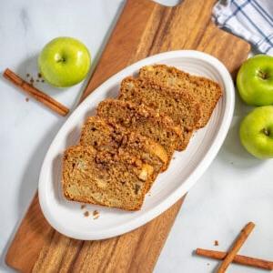 Apfel-Zimt-Brot 3 Geschnittenes Vollkorn-Apfelbrot mit Streuseln auf weißem Teller mit Granny Smith Äpfeln im Hintergrund.