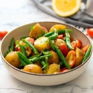 Italienischer Kartoffelsalat 4 Italienischer Kartoffelsalat in einer Schüssel, garniert mit frischer Petersilie, mit Tomaten im Hintergrund.