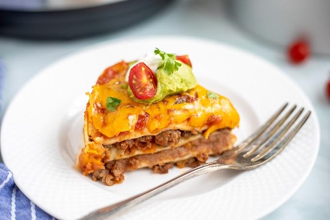 Ein Stück mexikanische Lasagne auf einem weißen Teller, garniert mit Tomate und Guacamole.