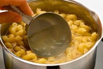 Nudelkochwasser wird mit einem Messbecher aus dem Topf mit kochenden Cavatappi-Nudeln abgeschöpft.