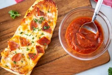 Baguette Pizza mit Peperoni auf einem Holzschneidebrett neben Pizzasoße.