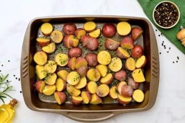 Halbierte rote Kartoffeln auf dem Backblech, gewürzt mit Knoblauchpulver, Salz, Pfeffer und Rosmarin.