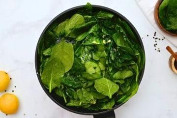 Frischer Spinat mit Knoblauch und Zitrone in einer großen Bratpfanne.