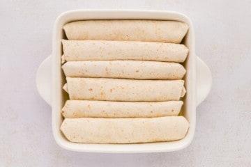 Mit zerkleinertem Hähnchen und Salsa Verde gefüllte Weizentortillas in einer weißen Auflaufform.