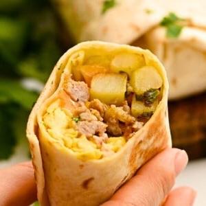 Aufgeschnittener Frühstücks-Burrito mit sichtbaren Eiern, Wurst und Kartoffeln im Inneren.