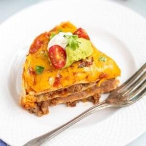 Ein Stück Instant Pot Taco Lasagne auf einem weißen Teller mit einem Instant Pot im Hintergrund.