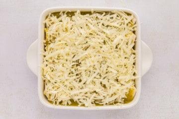 Gerollte Weizentortillas mit cremiger Hähnchenmischung, bedeckt mit grüner Salsa Verde und geriebenem Käse in einer weißen Auflaufform.