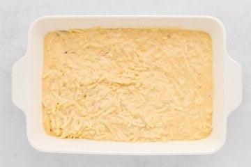 Geriebene Hash Browns mit hausgemachter Rahmsauce in einer Auflaufform verteilt.